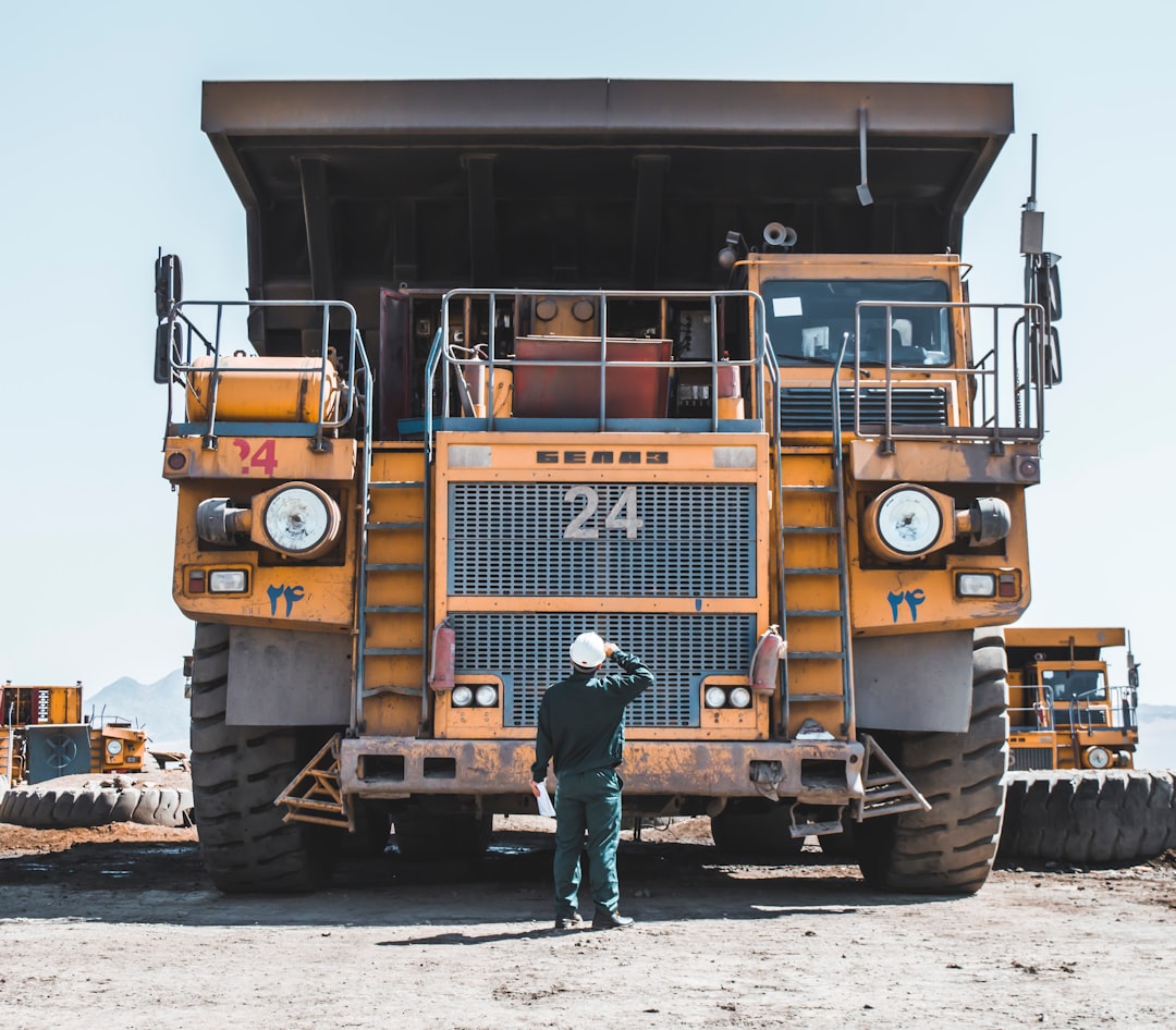 Photo by omid roshan man in brown jacket standing beside yellow truck
